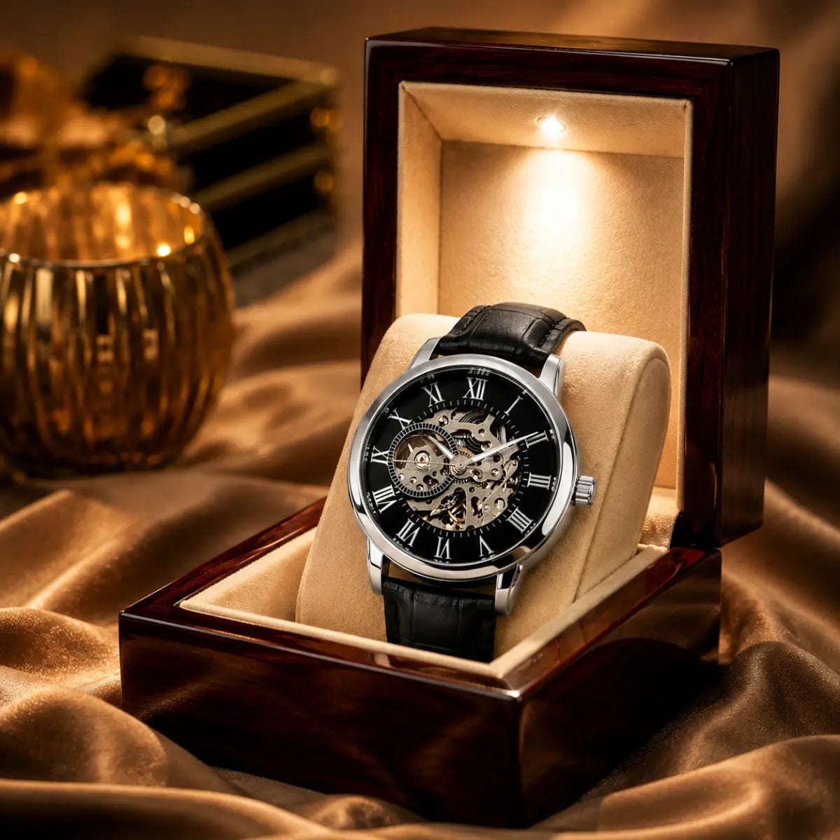 A luxury skeleton watch with a black leather strap and silver-tone case, displayed inside an open dark wood presentation box on a beige velvet cushion. The watch features a black dial with Roman numerals and a visible mechanical movement.