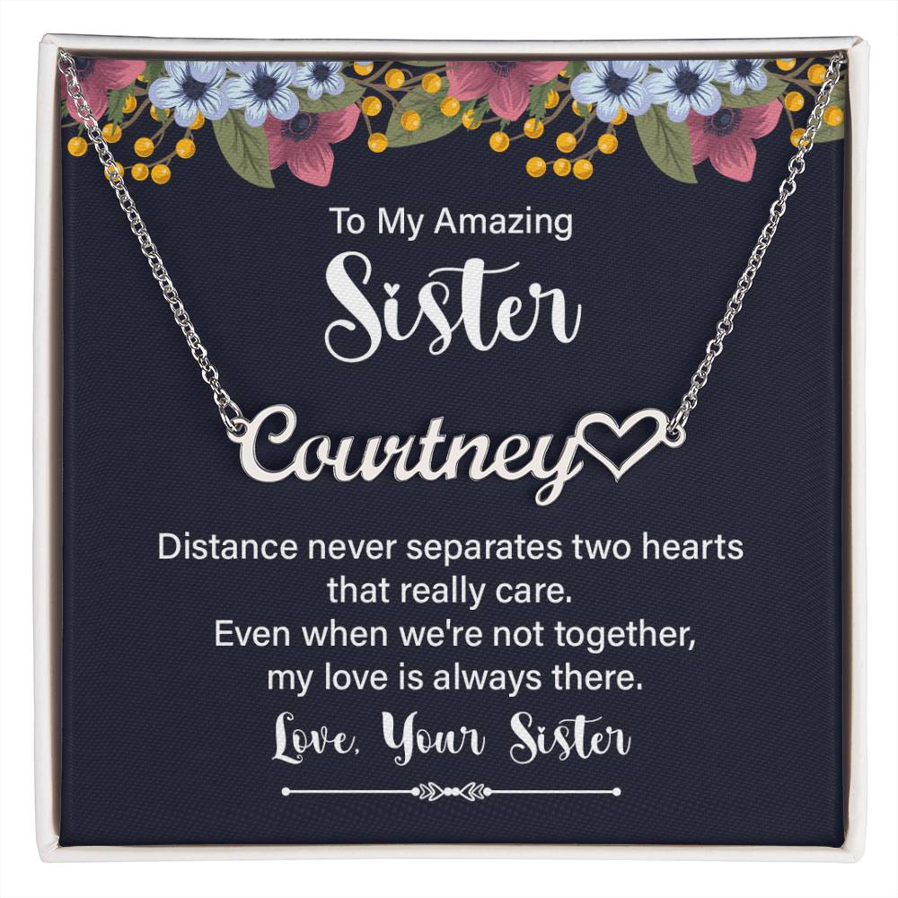 A floral jewelry card with a navy blue background, with a silver personalized cursive name necklace with a heart that says "TO MY AMAZING SISTER".