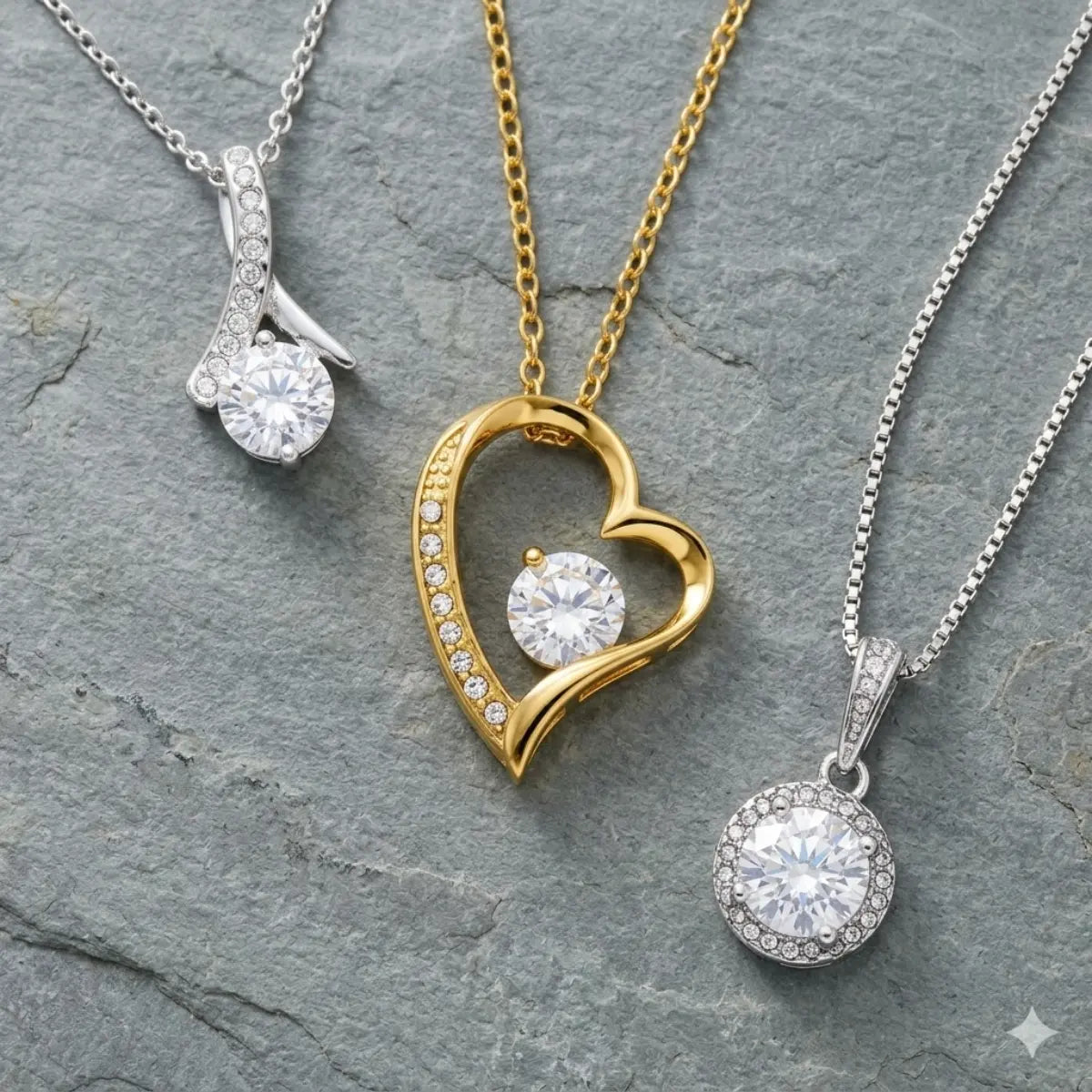 Three gold-plated pendant necklaces elegantly displayed on a gray stone surface: a silver ribbon pendant, a gold heart pendant, and a silver round halo pendant, each featuring a large brilliant-cut gemstone.