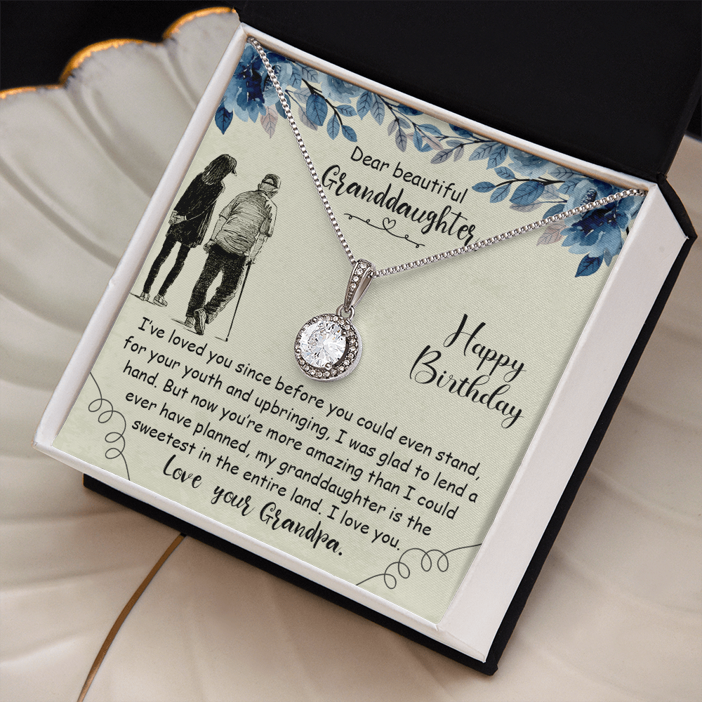 Personalized granddaughter birthday necklace on a cream floral gift card, sitting in a gold-trimmed ceramic leaf jewelry dish.
