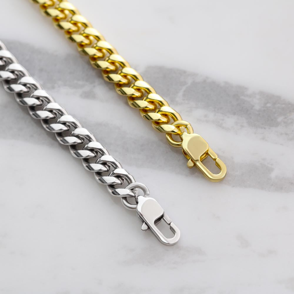 Two chain necklaces, one gold and one silver, on a marble surface.
