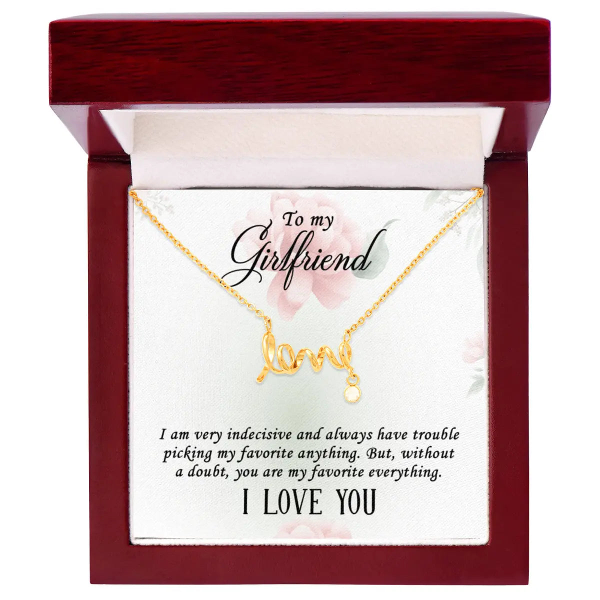 A silver 'I love you' initial necklace displayed on a white card inside a dark red wooden gift box. The card is addressed 'To my Girlfriend' and features a humorous quote, with the necklace hanging at the top.