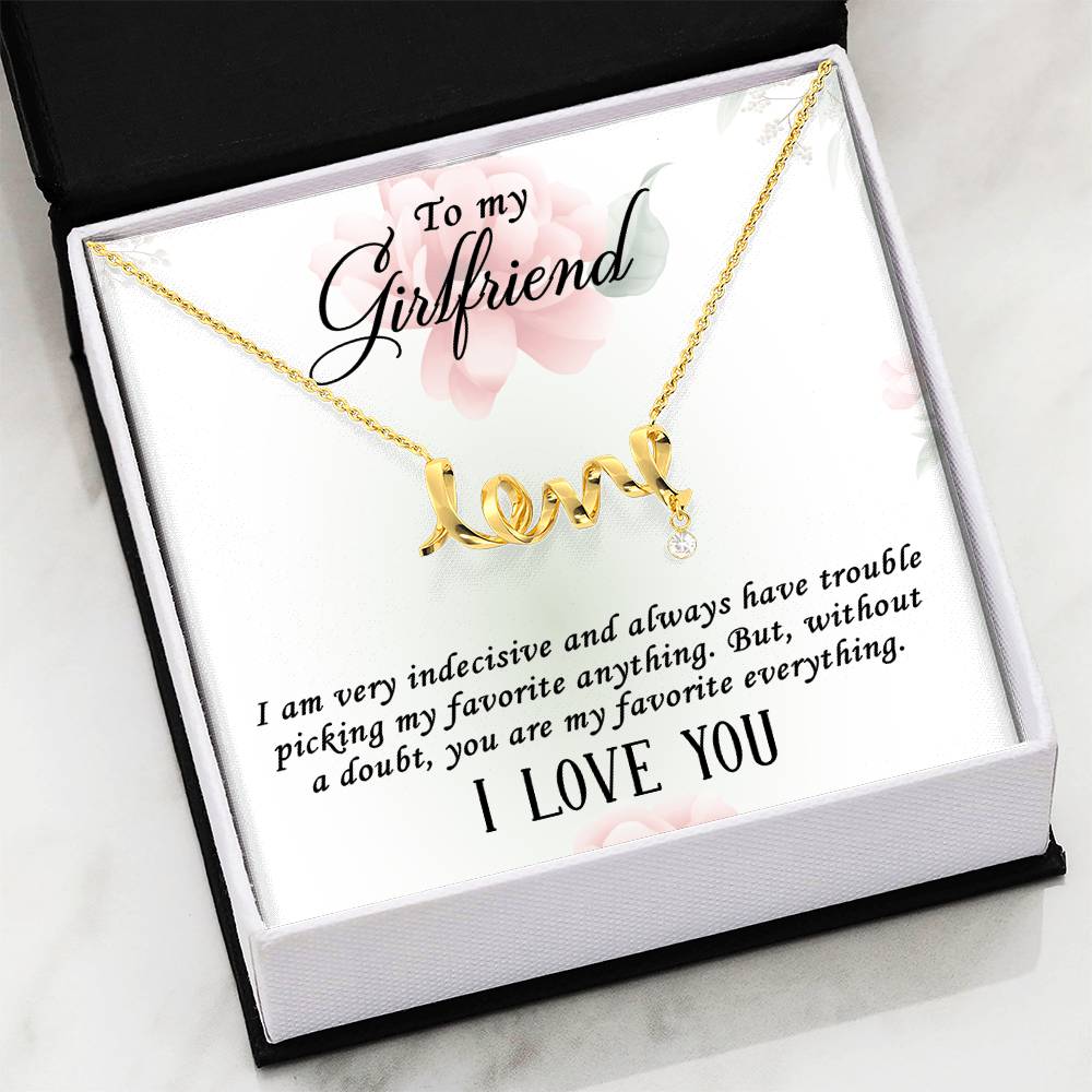 A gold necklace with a 'love' script pendant and a small teardrop charm, presented on a white gift card with floral accents and a message for a girlfriend in a black and white gift box.