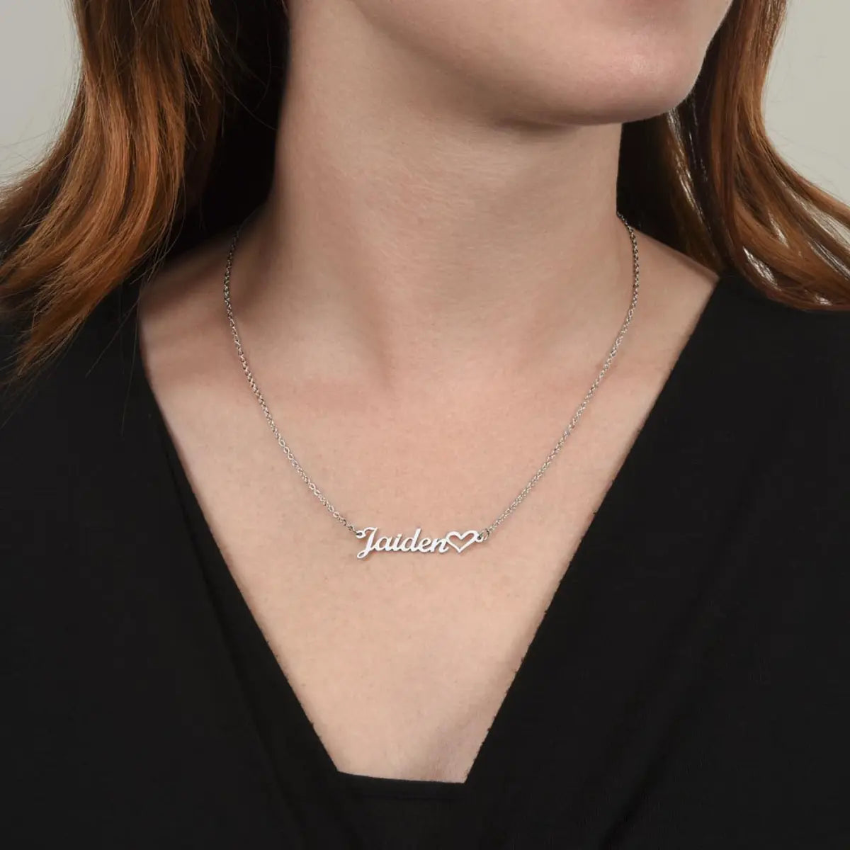 Person wearing a silver necklace with 'Jaiden' and a heart pendant on a plain background
