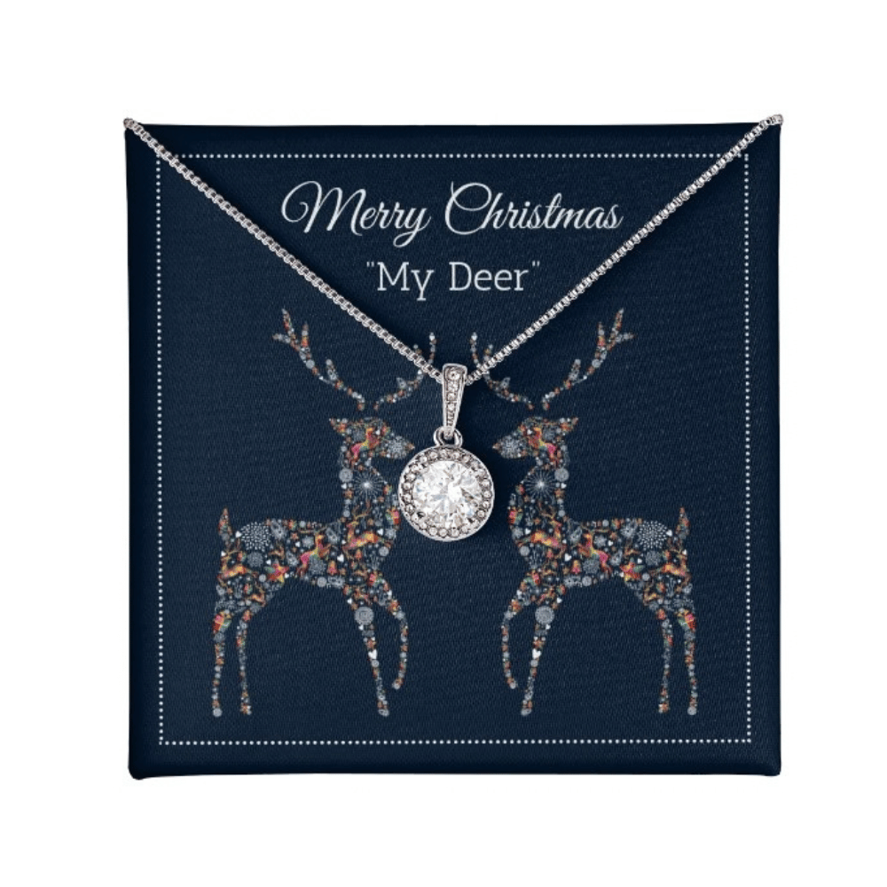 A silver-toned Christmas necklace with a round crystal-studded pendant, displayed on a navy blue gift card that reads "Merry Christmas 'My Deer'" and features two decorated deer illustrations.