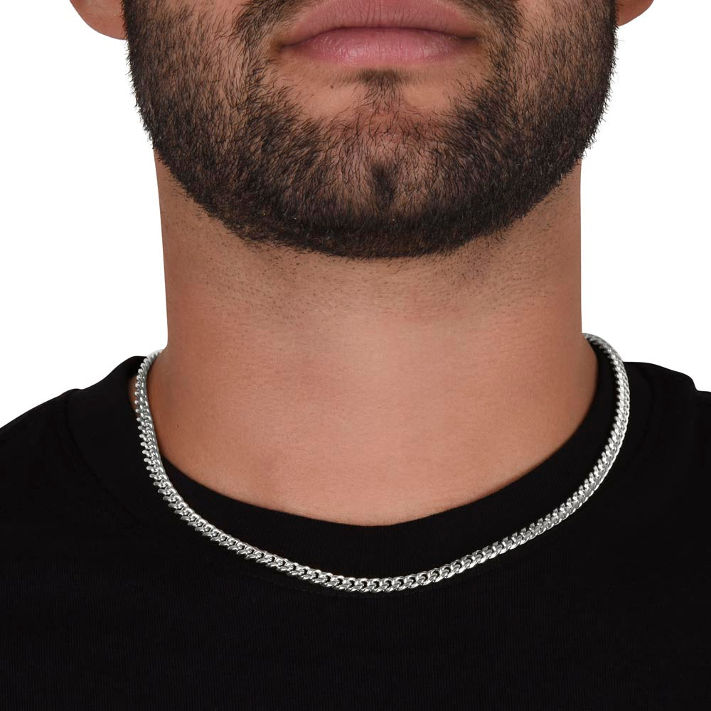 Man in a black shirt with a short black beard wearing a silver Cuban link chain round his neck.