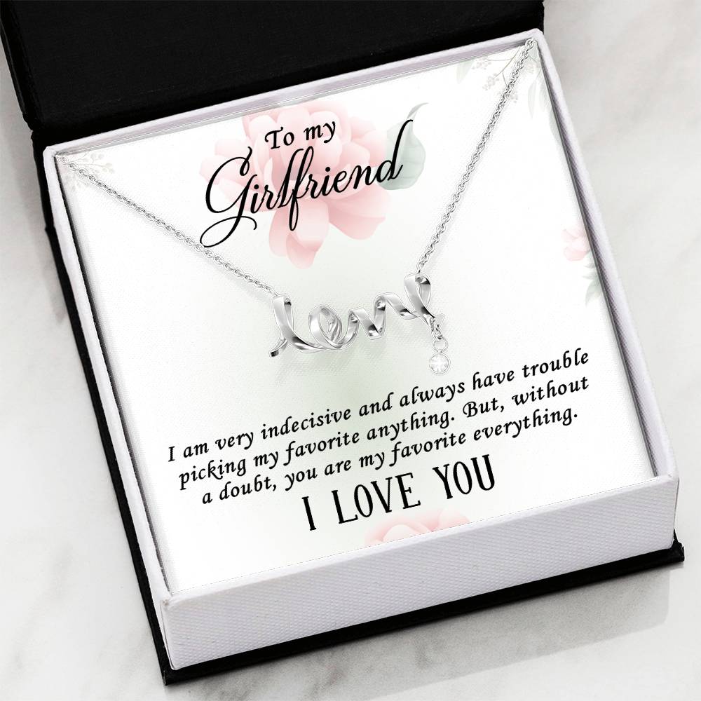 A silver necklace with a 'love' script pendant and a small teardrop charm, presented on a white gift card with floral accents and a message for a girlfriend in a black and white gift box.