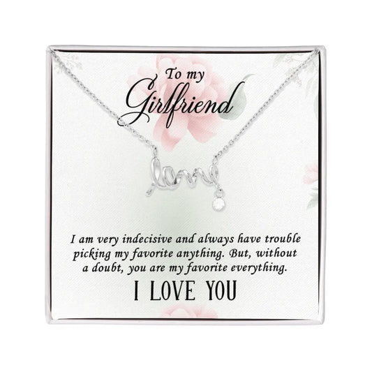 A silver necklace with a 'love' script pendant and a small teardrop charm, presented on a white gift card with floral accents and a message for a girlfriend.