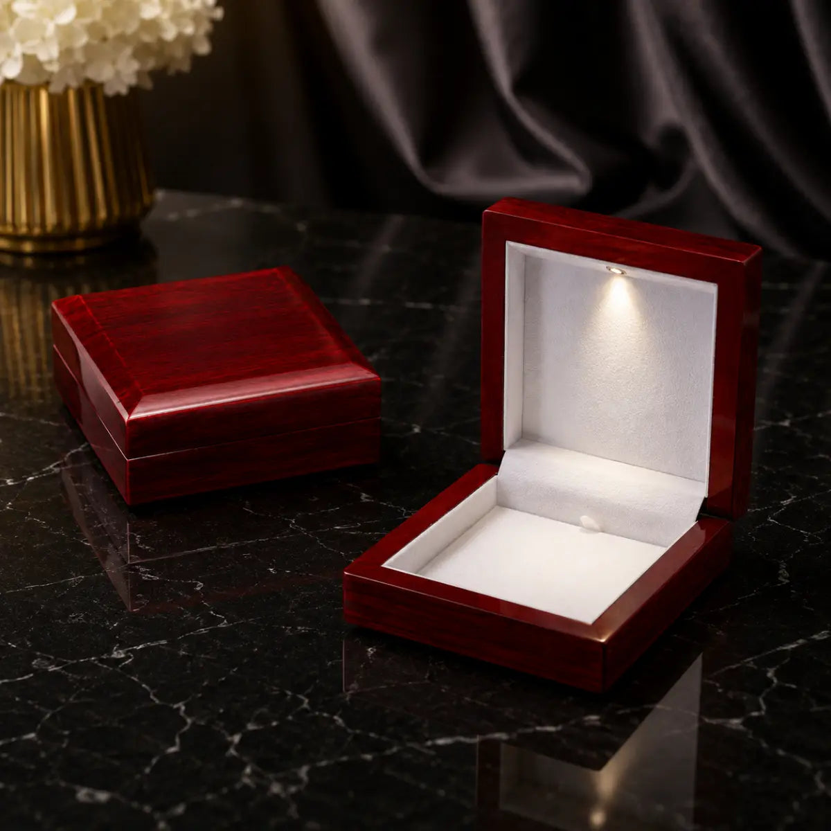 Two glossy dark red wooden jewelry boxes on a black marble surface, with one box open to show a white velvet interior and built-in LED light, and the other closed.