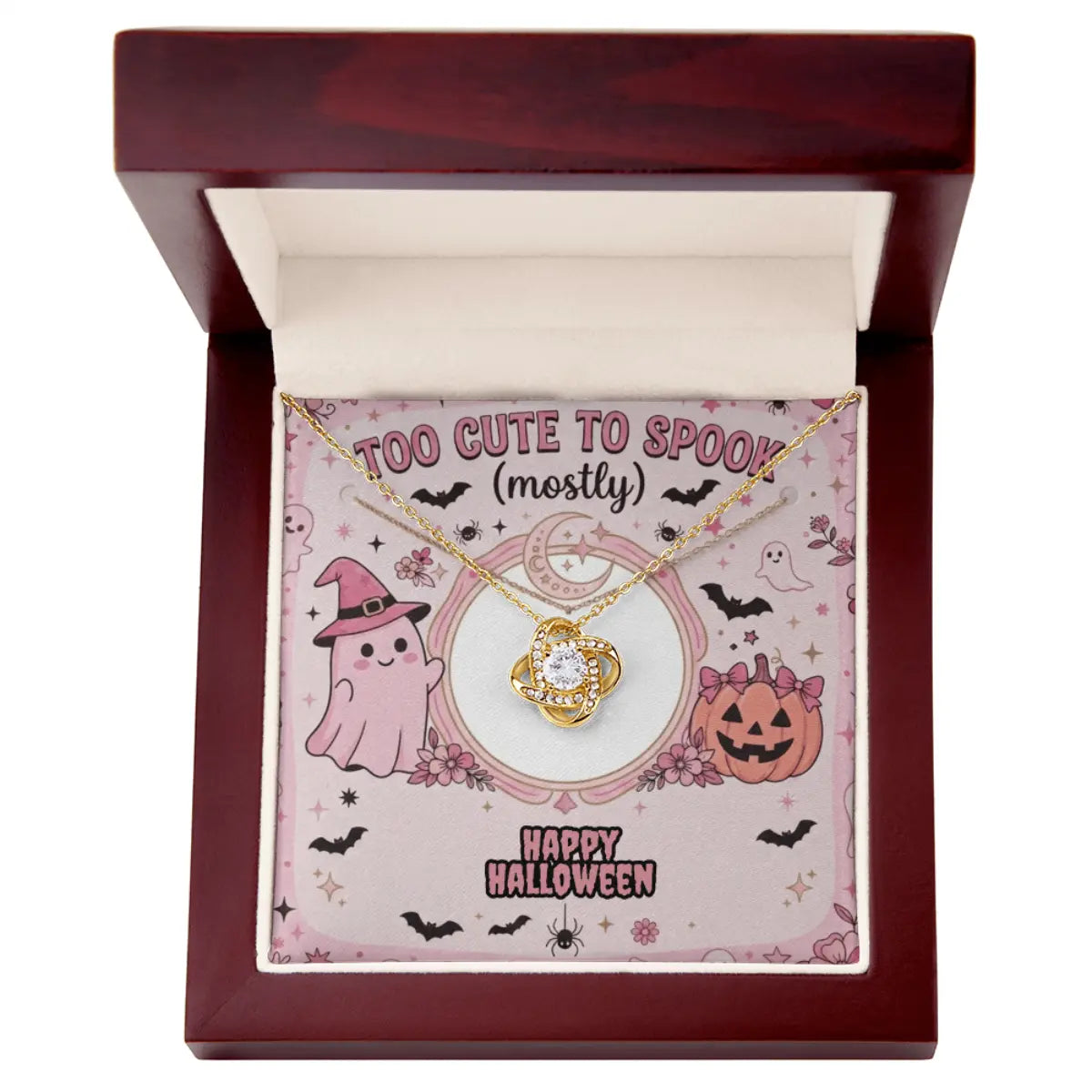 A gold  pendant necklace with cubic zirconia is displayed inside an open dark red wooden gift box. The necklace is presented on a pink Halloween-themed card with illustrations of a ghost, a pumpkin, and the text 'TOO CUTE TO SPOOK (mostly)' and 'HAPPY HALLOWEEN'.