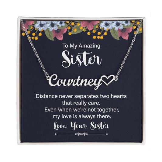 Personalized silver necklace with a heart-shaped nameplate, presented in a square gift box with a navy card featuring floral accents and a sentimental message for a sister.