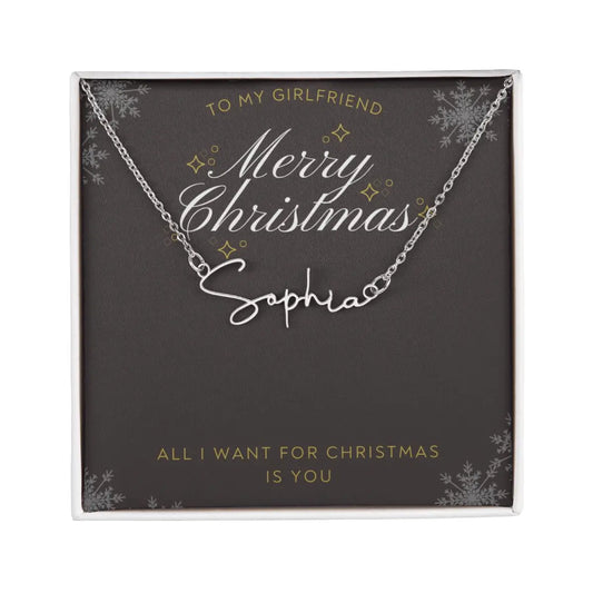 A personalized silver necklace with a script nameplate reading 'Sophia', presented on a dark gray square gift card with gold and white holiday text and snowflake designs. The card is addressed 'TO MY GIRLFRIEND' and reads 'Merry Christmas Sophia' and 'ALL I WANT FOR CHRISTMAS IS YOU'.