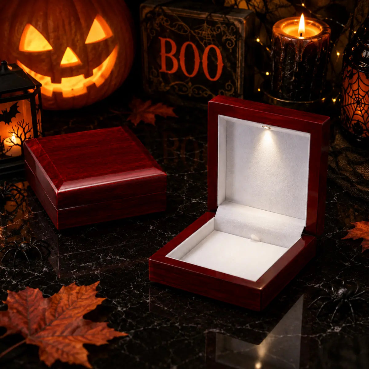 Two dark reddish-brown wooden jewelry boxes on a black reflective surface, one closed and one open showing a white interior with a built-in LED light. Halloween decorations including a jack-o'-lantern, candles, spiderwebs, and autumn leaves surround them.