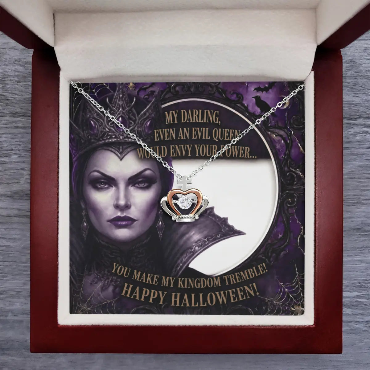 A silver and rose gold crown pendant necklace with a cubic zirconia is displayed on a printed card inside an open dark red gift box. The card features a gothic illustration of a queen with the text 'MY DARLING, EVEN AN EVIL QUEEN WOULD ENVY YOUR POWER.