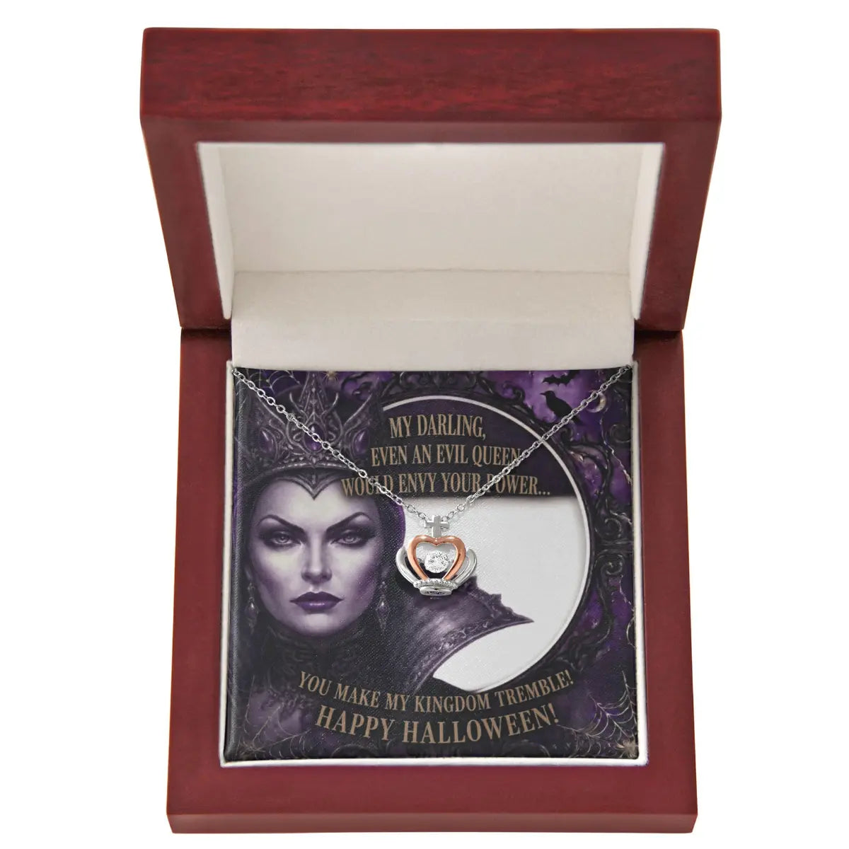 A silver and rose gold crown pendant with cubic zirconia necklace displayed inside an open reddish-brown wooden gift box. The necklace is laid over a printed card featuring a dark illustration with Halloween-themed text.