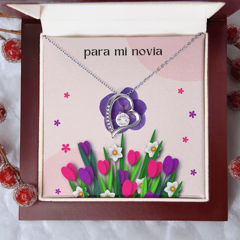 Collar plateado con dije de corazón y cristal brillante, presentado en una caja de madera de caoba abierta con una tarjeta de regalo floral rosa que dice "para mi novia".