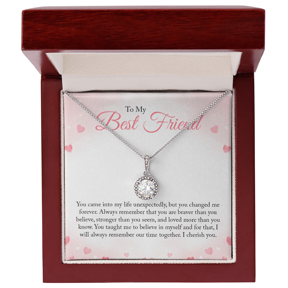 A round-cut cubic zirconia pendant necklace in white gold over a personalized 'To My Best Friend' sentimental message card with pink hearts in a dark red wooden gift box.