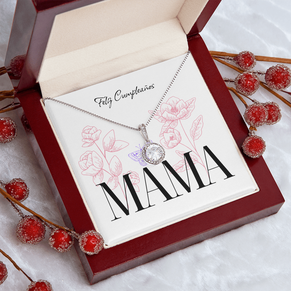 Vista en primer plano de un collar de plata con dije redondo brillante, presentado dentro de una elegante caja de madera caoba abierta. El collar descansa sobre la tarjeta blanca con el texto "Feliz Cumpleaños" y "MAMA", rodeado de decoraciones de ramas con pequeñas esferas rojas brillantes sobre un fondo blanco texturizado.