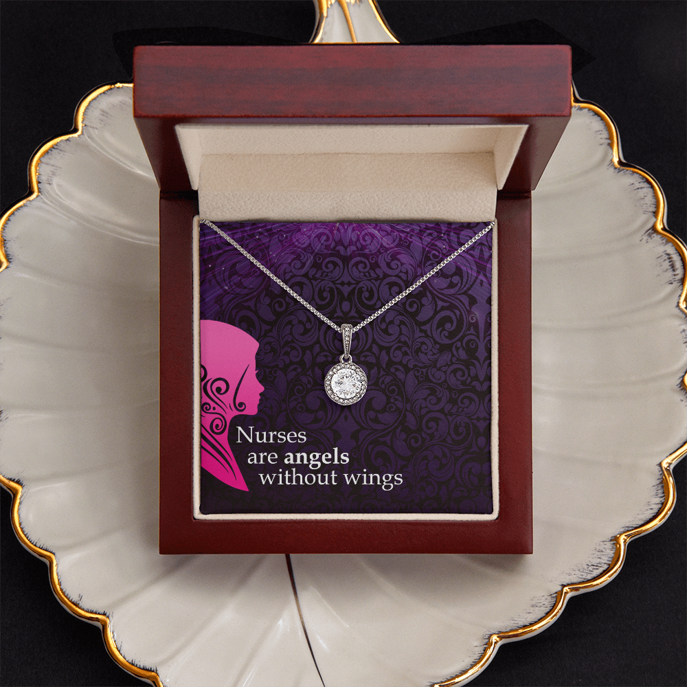 A silver chain necklace with a round, halo-set crystal pendant is presented inside an open wood jewelry box with a dark border on a cream and gold trimmed shell jewelry dish. The necklace rests against a decorative purple card with a damask pattern, a pink nurse silhouette, and the white text, "Nurses are angels without wings."