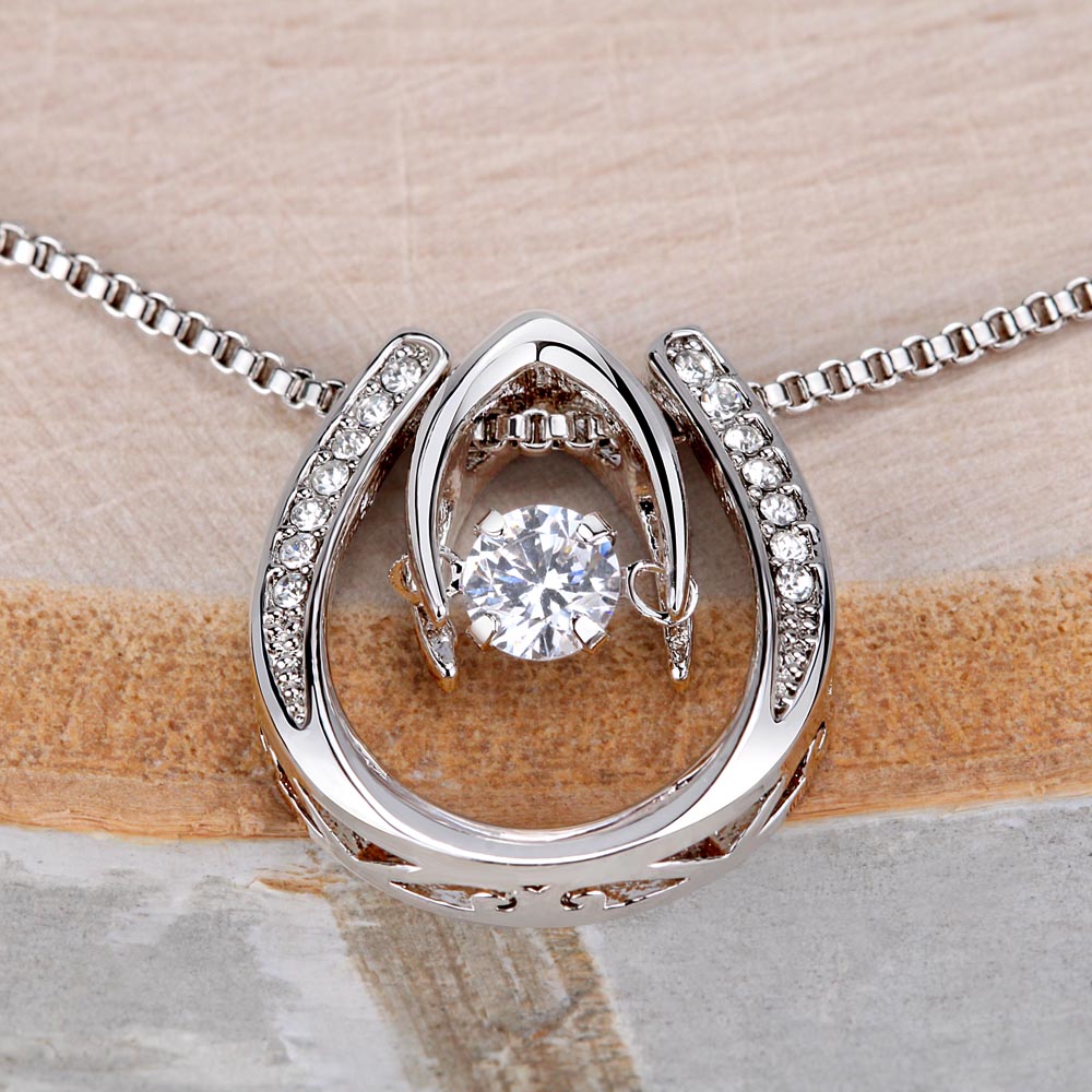 Extreme close-up shot of a silver horseshoe pendant necklace featuring an outer horseshoe ring lined with small stones and a large dancing cubic zirconia crystal suspended in the center.