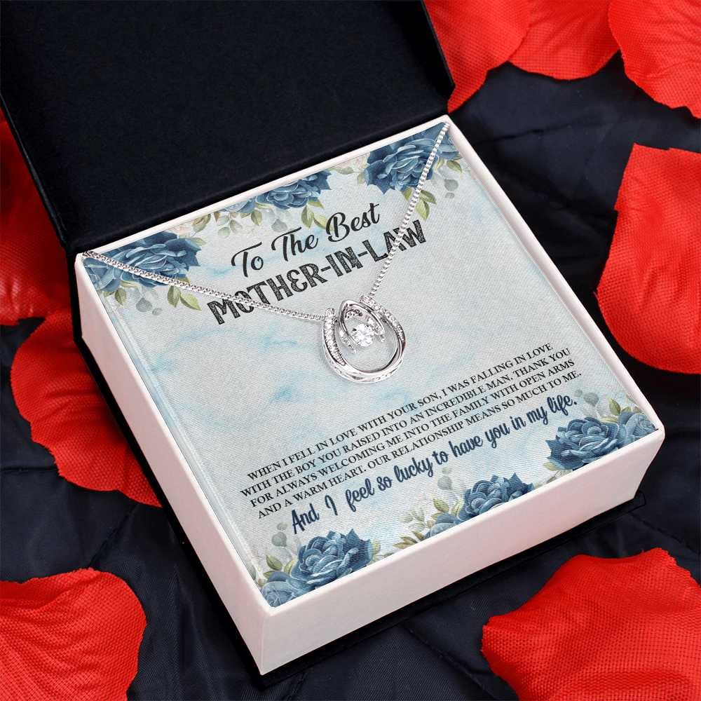 Silver horseshoe pendant necklace with a dancing crystal center, displayed inside an open gift box on a blue floral message card for a mother-in-law, surrounded by decorative red rose petals.