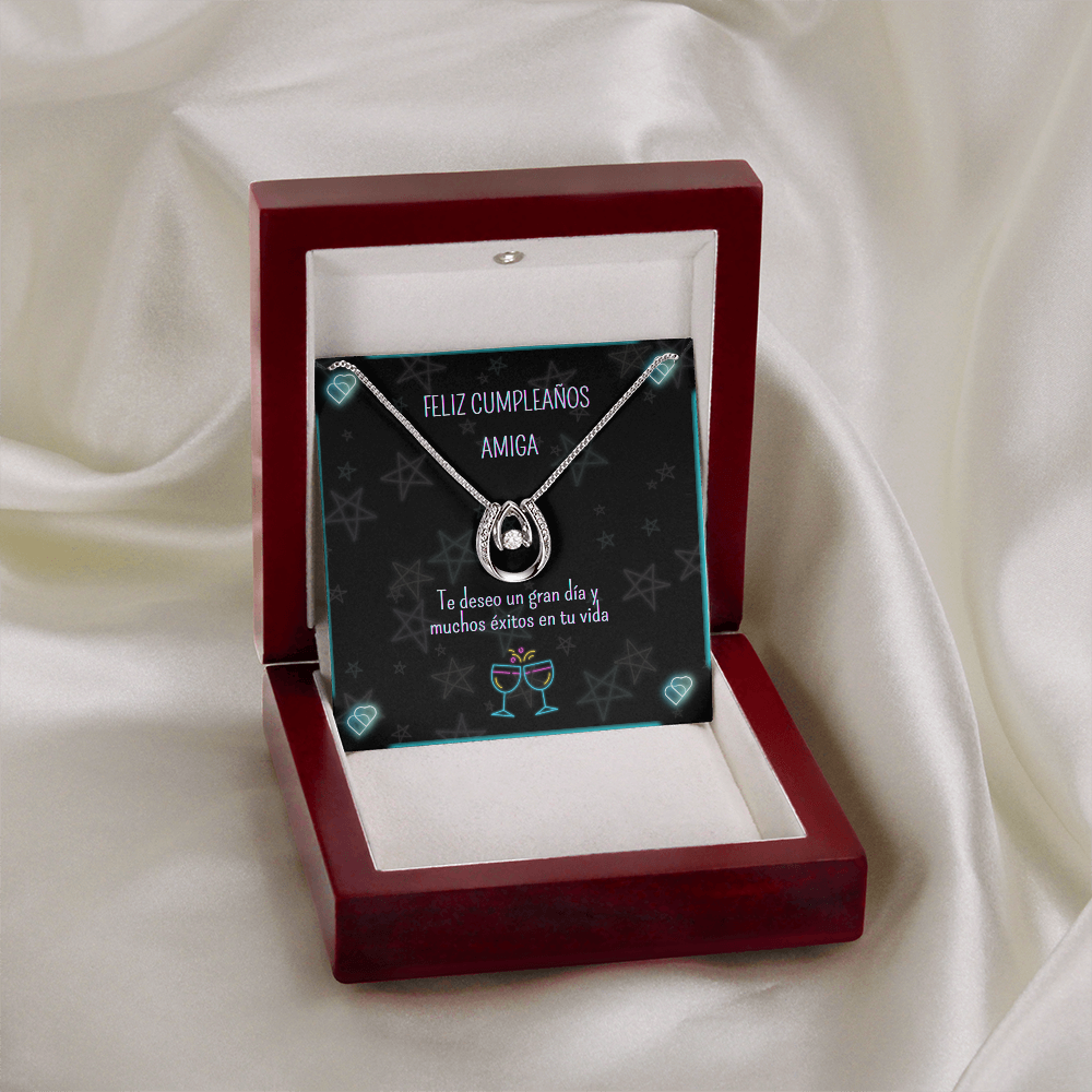 Collar de herradura plateado con piedra brillante, presentado en una caja de madera de lujo abierta con luz LED integrada encendida sobre la tarjeta de regalo. El conjunto descansa sobre un fondo de tela de satén blanco satinado con pliegues suaves.