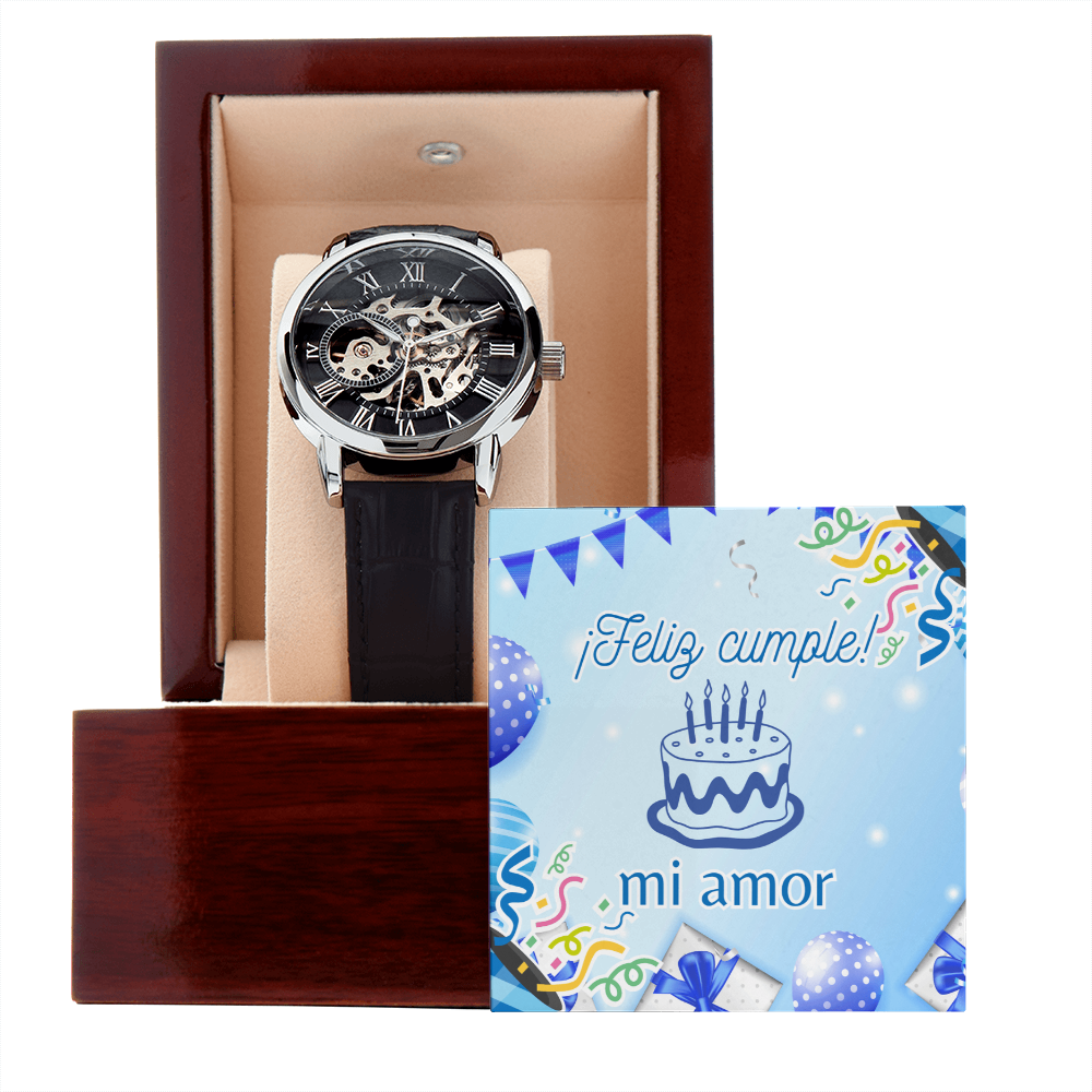 Reloj automático tipo skeleton para hombre con correa negra, exhibido dentro de un estuche de madera premium con interior beige, junto a una tarjeta de felicitación azul que dice ¡Feliz cumple mi amor!