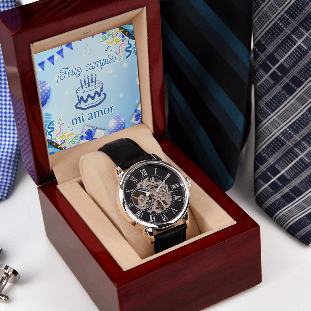 Reloj mecánico skeleton para hombre con bisel color oro rosa y correa negra, colocado en su estuche de madera abierta junto a corbatas elegantes y una tarjeta integrada que dice ¡Feliz cumple mi amor!