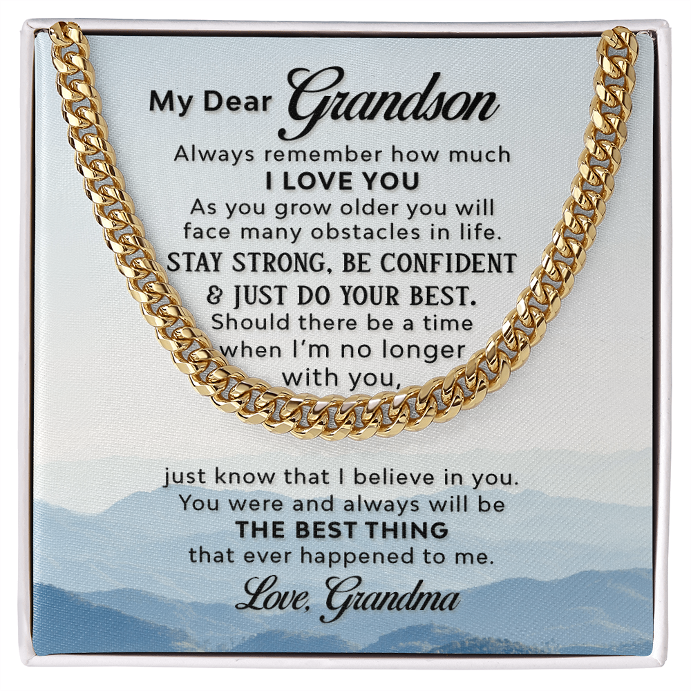 A gold-colored men's Cuban link chain necklace draped over a square white message card inside a gift box. The background of the card features a scenic, misty blue mountain landscape.