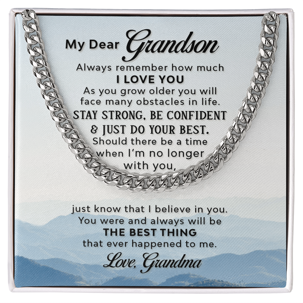 A silver-colored men's Cuban link chain necklace draped over a square white message card inside a gift box. The background of the card features a scenic, misty blue mountain landscape.