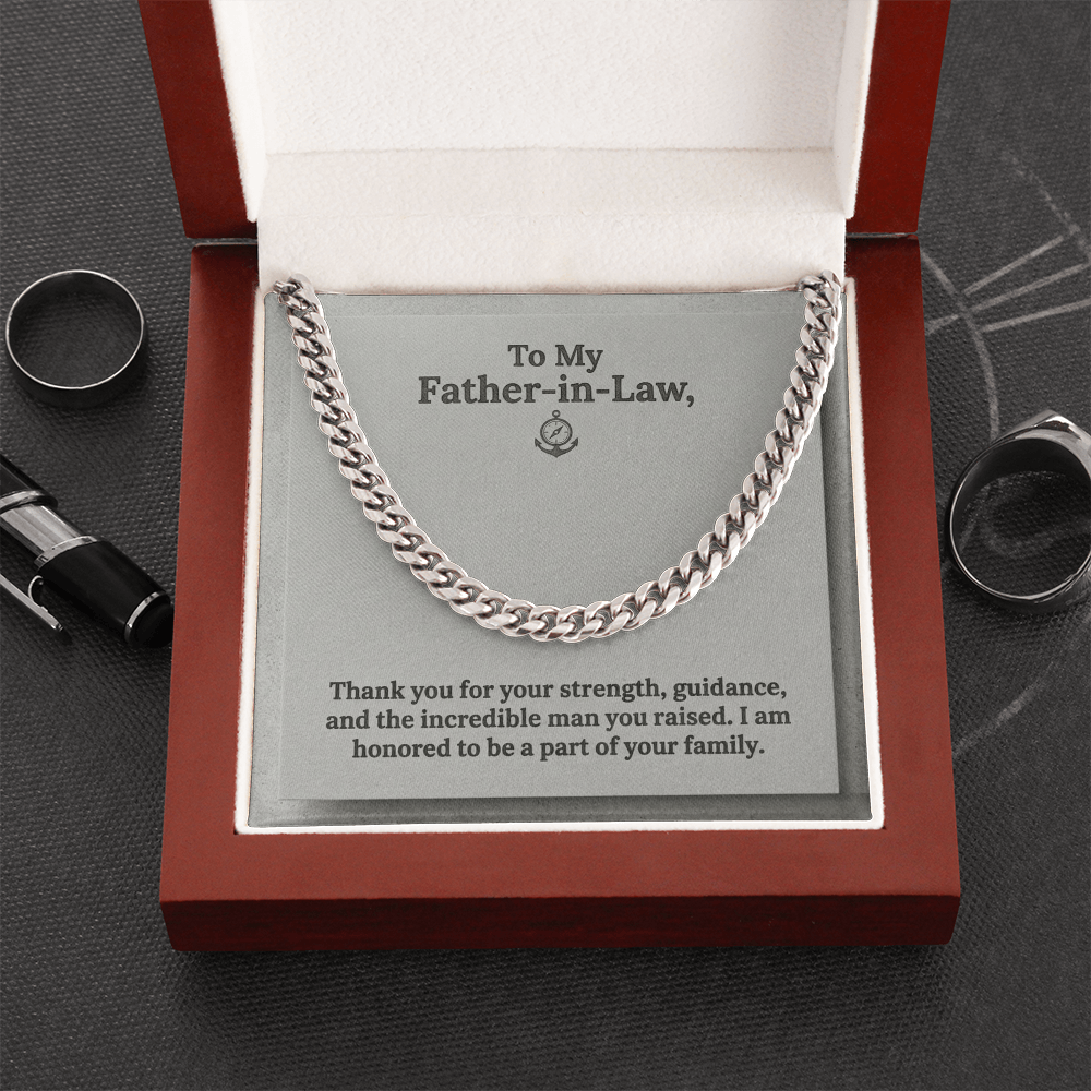 A silver-toned men's Cuban link chain necklace displayed inside an open luxury wooden gift box with a white interior. The necklace sits on a grey message card featuring a small anchor and compass logo and the printed text: "To My Father-in-Law, Thank you for your strength, guidance, and the incredible man you raised. I am honored to be a part of your family."