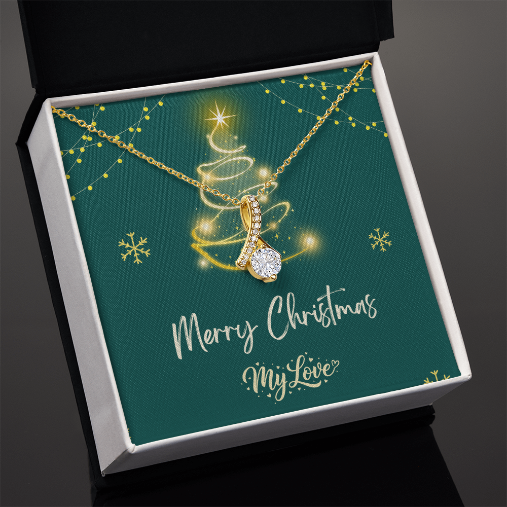 A gold Christmas tree pendant necklace with a sparkling clear teardrop-shaped center stone, presented on a dark green square gift card inside a black and white box. The card features a gold glittery Christmas tree, snowflakes, and the text 'Merry Christmas My Love."