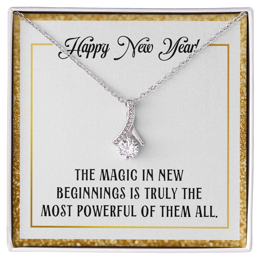 A silver-colored pendant necklace featuring a large, round-cut central crystal dangling from a ribbon-shaped bail encrusted with smaller crystals. The necklace is displayed inside a square white gift box with a sparkling gold glitter border. The necklace rests on a white card that reads "Happy New Year!" at the top in cursive and "THE MAGIC IN NEW BEGINNINGS IS TRULY THE MOST POWERFUL OF THEM ALL." at the bottom in bold, uppercase block lettering.
