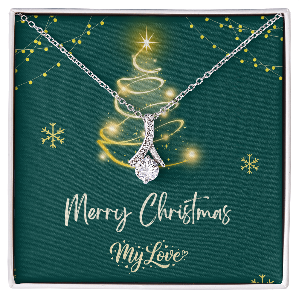 A silver Christmas tree pendant necklace with a sparkling clear teardrop-shaped center stone, presented on a dark green square gift card inside a white box. The card features a gold glittery Christmas tree, snowflakes, and the text 'Merry Christmas My Love."