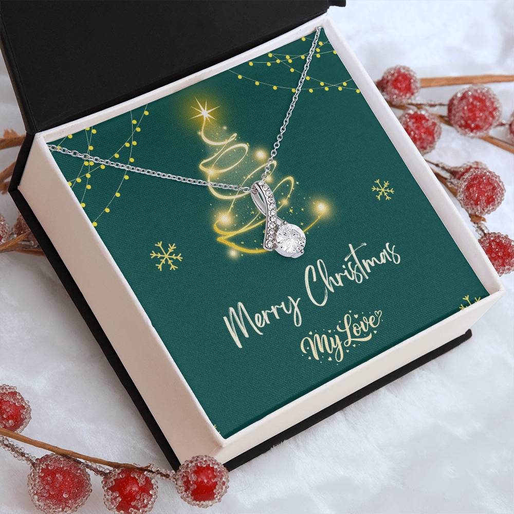 A silver Christmas tree pendant necklace with a sparkling clear teardrop-shaped center stone, presented on a dark green square gift card inside a white box. The card features a gold glittery Christmas tree, snowflakes, red Christmas sugar berries, and the text 'Merry Christmas My Love."