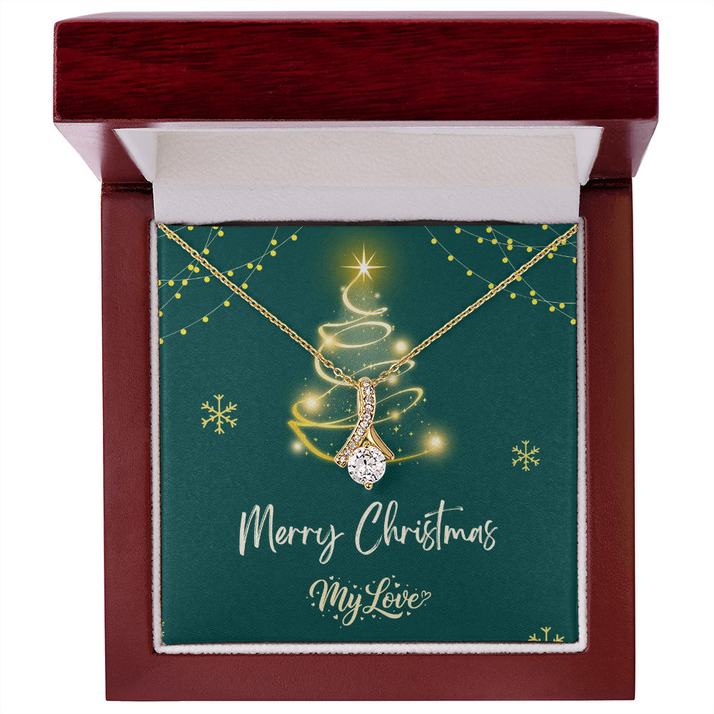 A gold Christmas tree pendant necklace with a sparkling clear teardrop-shaped center stone, presented on a dark green square gift card inside a white box. The card features a gold glittery Christmas tree, snowflakes, and the text 'Merry Christmas My Love."