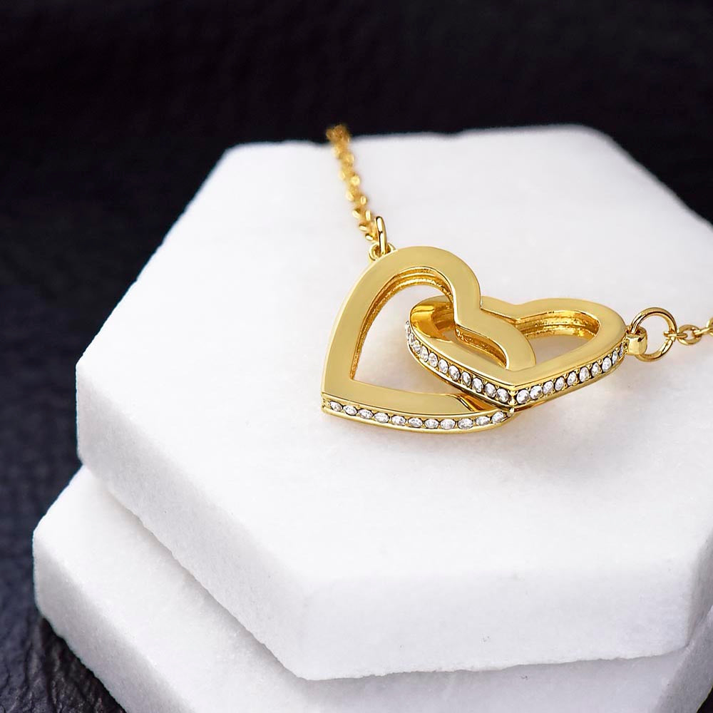 A gold-toned interlocking hearts necklace pendant with cubic zirconia laying on top of a double white pedestal display.