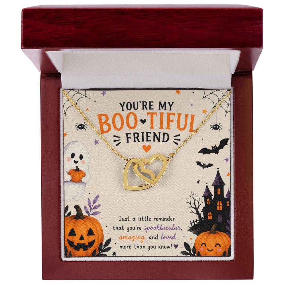 A Halloween-themed gift card featuring two gold-tone interlocking heart pendant necklace with cubic zirconia. The card is decorated with spooky illustrations including a ghost, jack-o'-lanterns, a haunted house, bats, and spiders, with the text 'YOU'RE MY BOOTIFUL FRIEND', in a luxury wooden LED spotlight gift box.