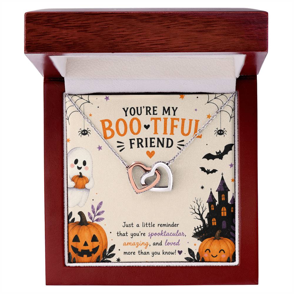 A Halloween-themed gift card featuring a silver and rose gold two-tone interlocking heart pendant necklace with cubic zirconia. The card is decorated with spooky illustrations including a ghost, jack-o'-lanterns, a haunted house, bats, and spiders, with the text 'YOU'RE MY BOOTIFUL FRIEND', in a luxury wooden gift box.