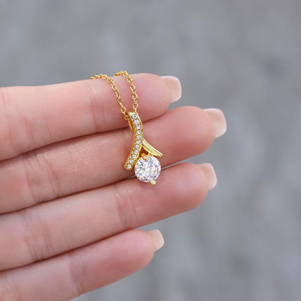 A gold Christmas pendant necklace with a sparkling clear teardrop-shaped center stone displayed on a woman's hand.