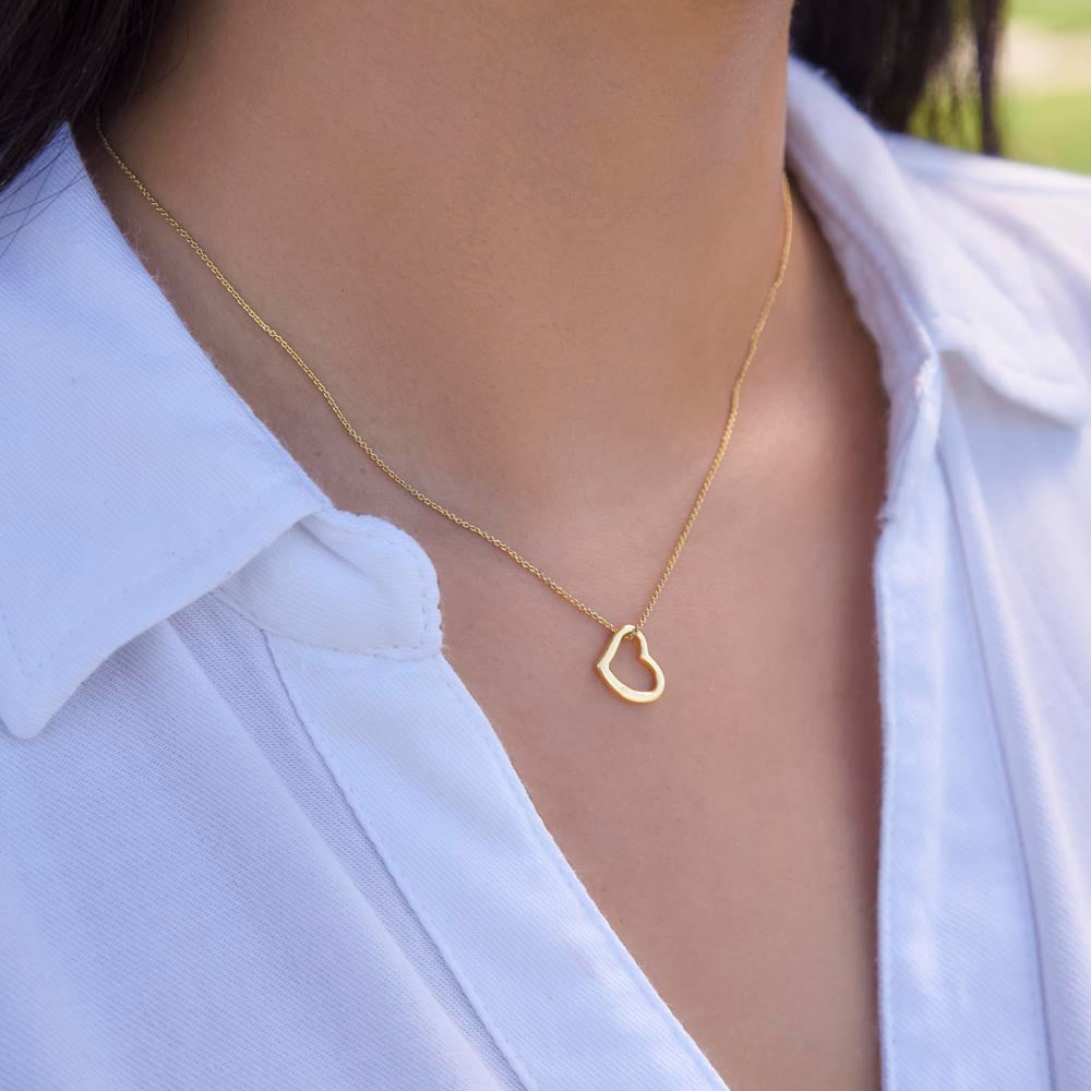 A model wearing a delicate 18k gold open heart necklace paired with a crisp white button-down shirt for a minimalist everyday look.