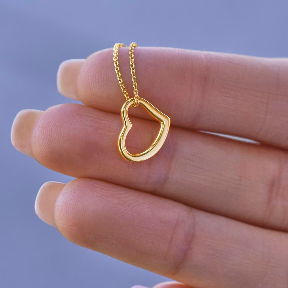 A close-up shot of a delicate 18k gold open heart necklace resting gently on a person's fingers to show scale.