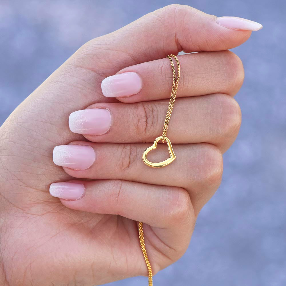 A close-up view of a woman's hand with a pink and white ombre manicure holding the delicate 18k gold open heart necklace to showcase the fine chain details.