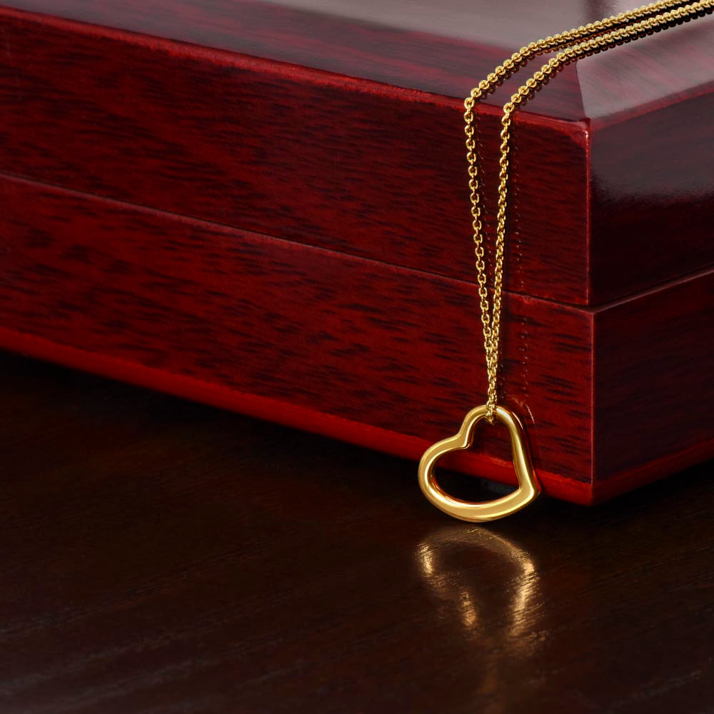A close-up shot of the delicate 18k gold open heart necklace draped over the edge of a polished mahogany wood gift box.