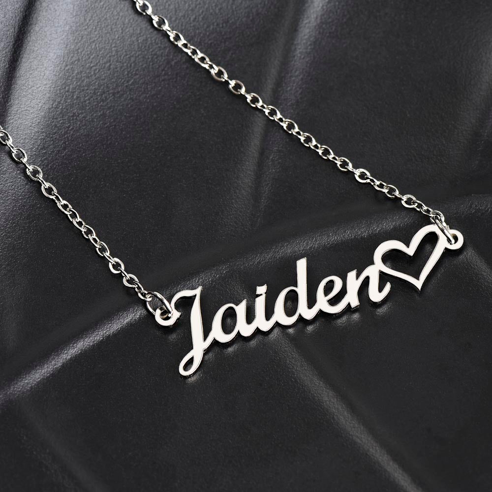 Personalized silver necklace with a heart-shaped nameplate, presented on a black leather material.