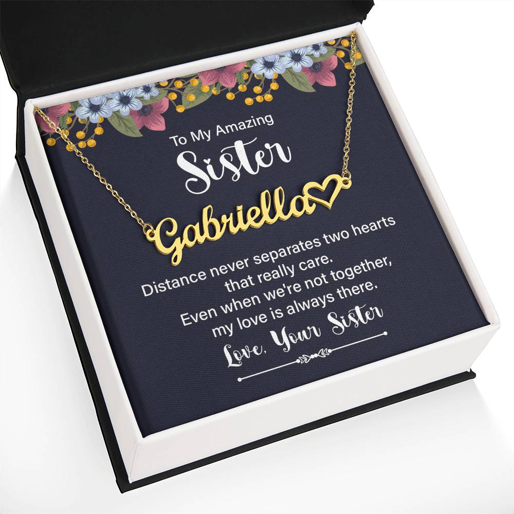 Personalized gold necklace with a heart-shaped nameplate, presented in a square gift box with a navy card featuring floral accents and a sentimental message for a sister.
