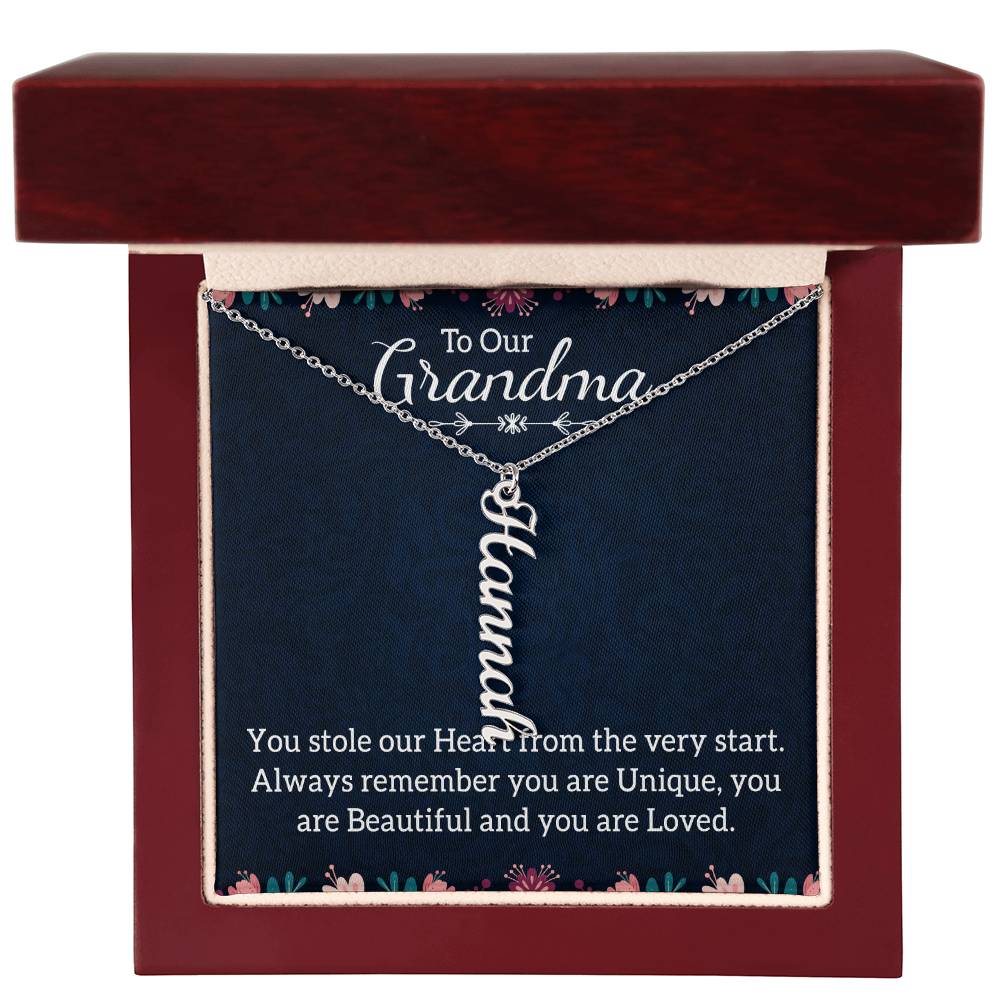 A personalized silver nameplate necklace displayed on a dark navy gift card with floral accents and a sentimental message for 'Grandma', in a dark wooden gift box with a white background.