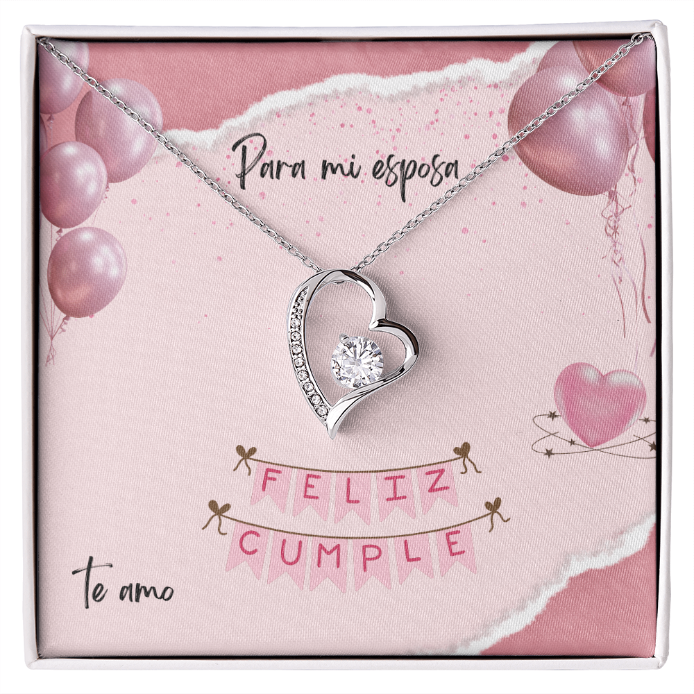 Collar con dije de corazón y cristal brillante sobre una tarjeta de regalo rosa que dice "Para mi esposa, Feliz Cumple, Te amo" decorada con globos.