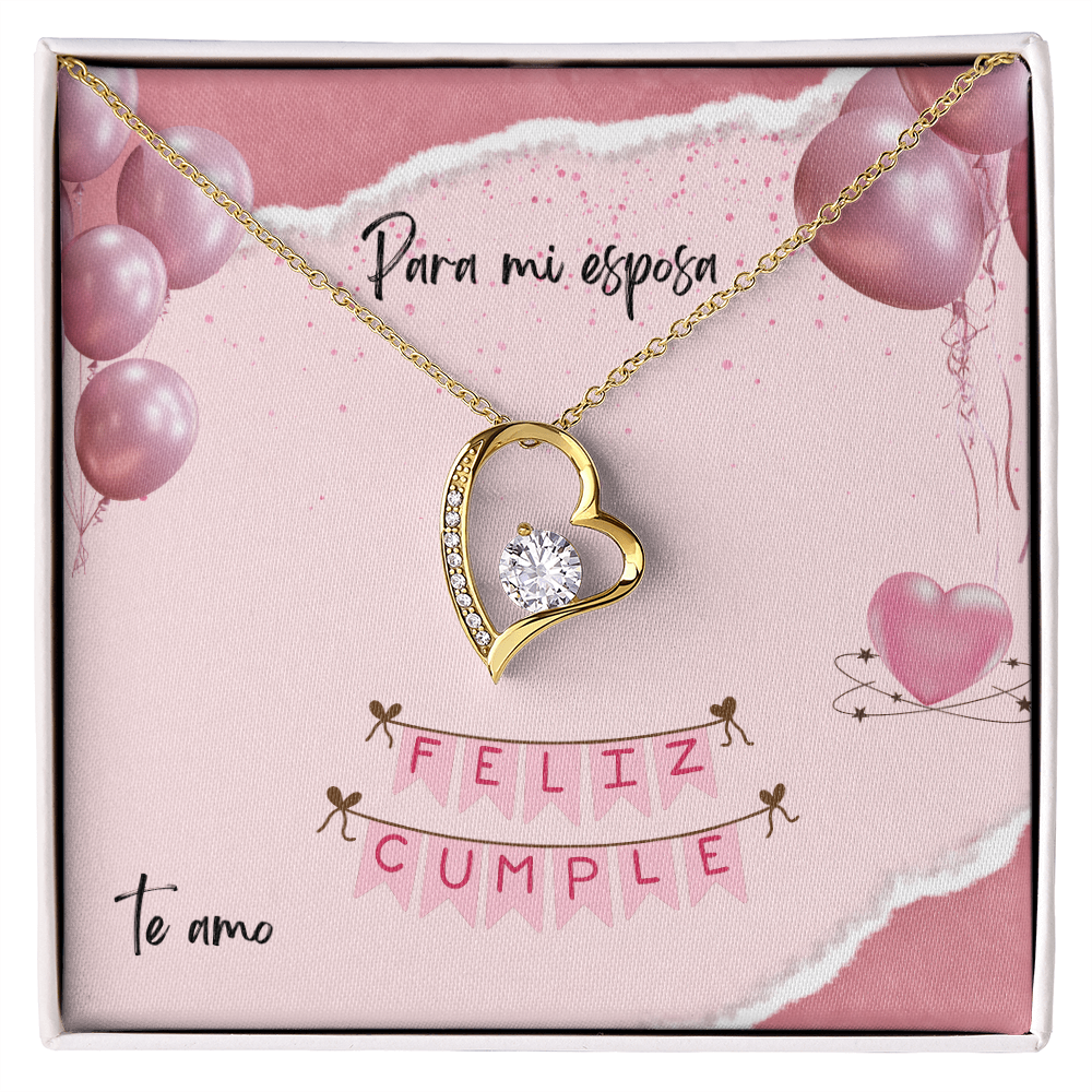 Collar de oro con dije de corazón y cristal brillante sobre una tarjeta de regalo rosa que dice "Para mi esposa, Feliz Cumple, Te amo" decorada con globos.