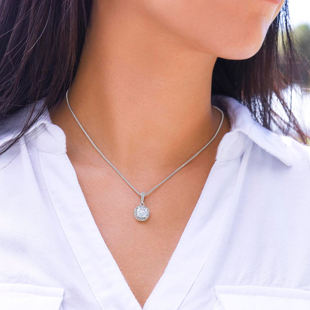A close-up of a woman wearing a silver round halo pendant necklace with a sparkling central stone, paired with a white button-up shirt.